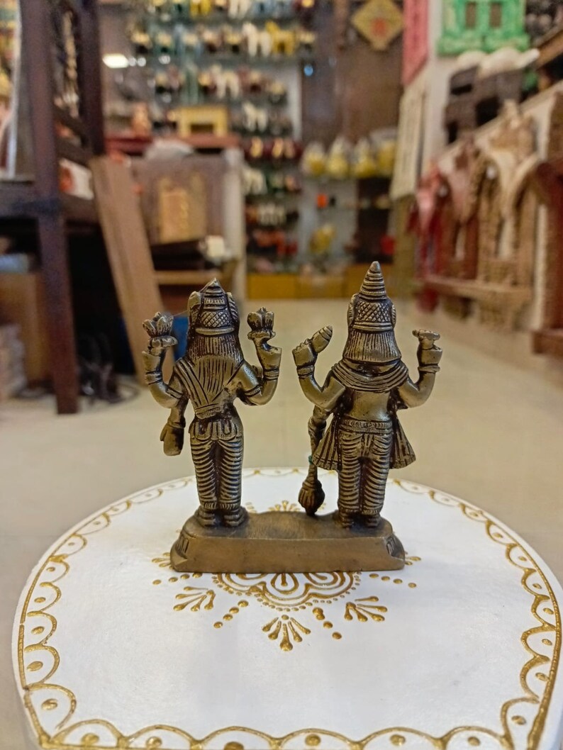 May include: A brass figurine of two deities standing back to back. The figurine is on a white circular base with gold painted designs.