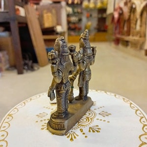 May include: A gold-colored metal figurine of two deities standing back to back. The figurine is on a white base with gold painted designs.