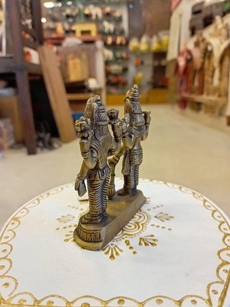 May include: A gold-colored metal figurine of two deities standing back to back. The figurine is on a white base with gold painted designs.