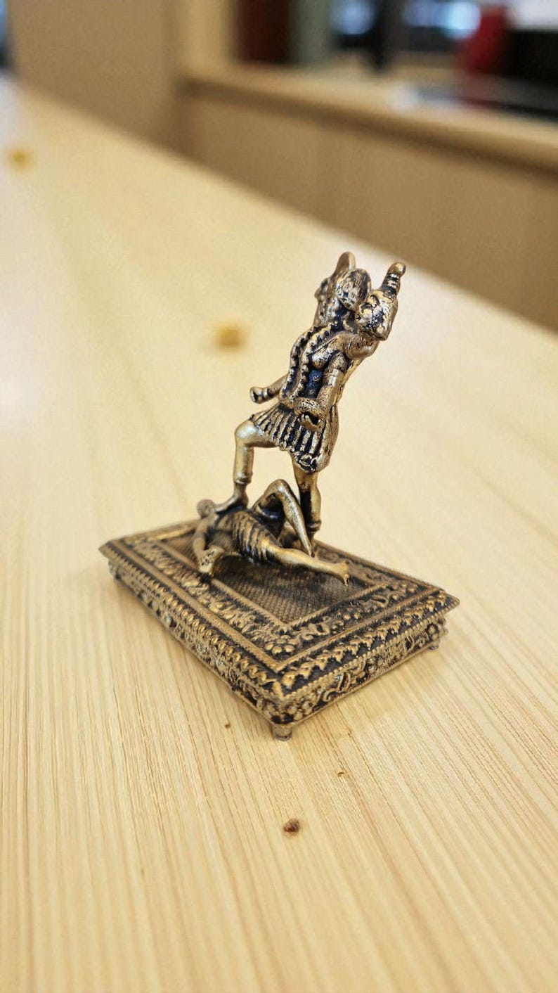 May include: A bronze-coloured figurine showing a figure standing over another on a rectangular base. The standing figure is in a dynamic pose, with one leg raised. The base has intricate patterns. The overall theme is historical or mythological.