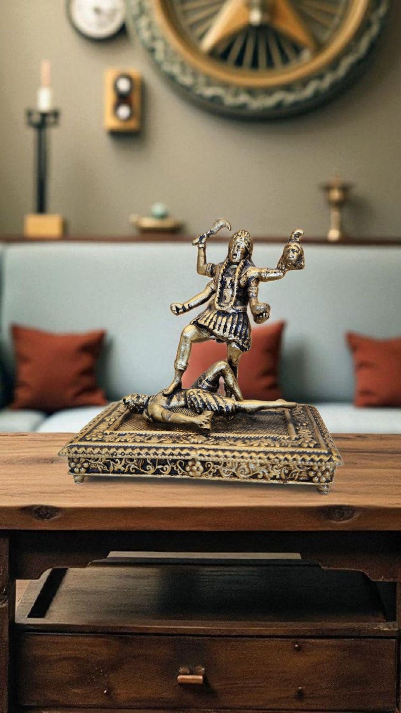 May include: A bronze-coloured statue of a multi-armed figure standing on a figure lying down. The statue is on a decorative base with intricate patterns. The figure holds a sword and a severed head.