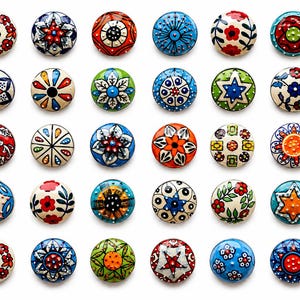 Puede incluir: Una colección de treinta pomos de cerámica redondos dispuestos en una cuadrícula, cada uno con patrones únicos pintados a mano en colores vibrantes como rojo, azul, verde, naranja y amarillo, con intrincados diseños florales, geométricos y de estrellas.