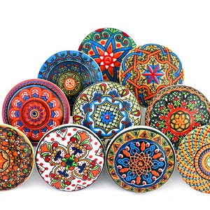 May include: A collection of eleven decorative ceramic cabinet knobs. Each knob features a unique, colorful, and intricate pattern in shades of blue, orange, red, green, and yellow. The knobs are round and have a glossy finish, perfect for adding a touch of artistry to furniture.