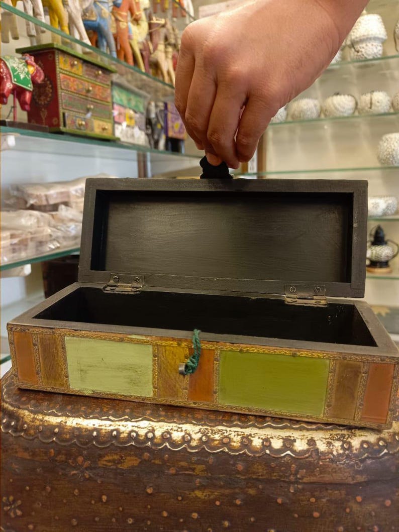 Puede incluir: Una caja de madera con tapa con bisagras y un dise&ntilde;o geom&eacute;trico colorido. La caja est&aacute; abierta y el interior est&aacute; vac&iacute;o.