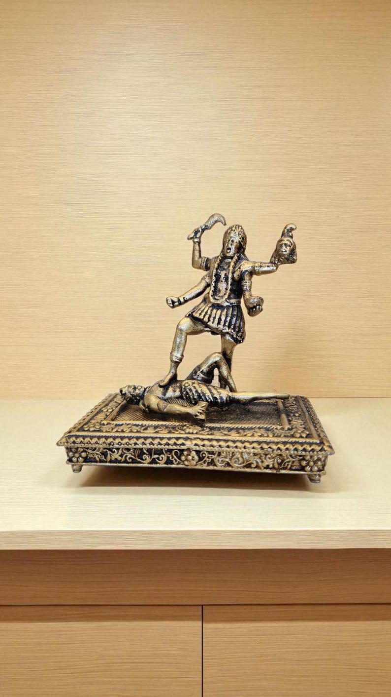 May include: A bronze-coloured statue of a multi-armed deity standing on a figure, holding a sword and a severed head. The statue is on a decorative, rectangular base with ornate detailing.