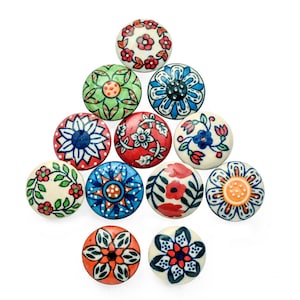 Peut inclure: Une collection de onze boutons de placard ronds en céramique avec des motifs floraux peints à la main. Les boutons présentent diverses couleurs, dont le rouge, le bleu, le vert et l'orange, avec des fonds blancs. Chaque bouton a un motif floral unique.