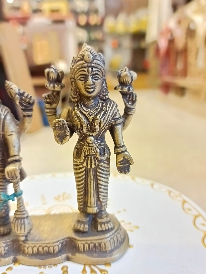 May include: A gold-colored metal statue of a Hindu deity with four arms, holding a lotus flower in each hand. The statue is standing on a base with intricate details.