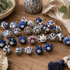 May include: A collection of round ceramic cabinet knobs featuring various blue, white, and red hand-painted floral, geometric, and striped patterns. Each knob has a central silver-toned metal hardware fitting for attachment to furniture drawers or doors.