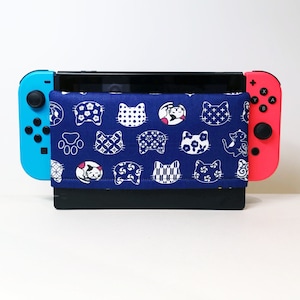 May include: A blue and white patterned Nintendo Switch case with a blue and red Nintendo Switch console. The case features a repeating pattern of cats and paw prints.