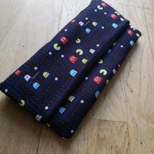 May include: Black clutch bag with a Pac-Man pattern. The bag has a zip fastening and a black lining.