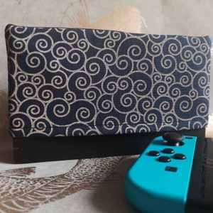 Puede incluir: Una funda de tela negra y blanca para una consola Nintendo Switch. La funda tiene un mando Nintendo Switch azul y turquesa con una placa frontal negra.