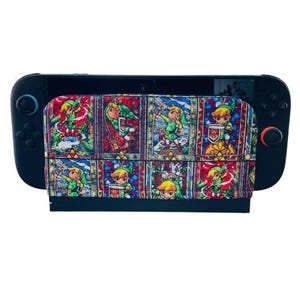 May include: A black Nintendo Switch console with a colorful case featuring a stained-glass style design. The case showcases a repeating pattern of a character in green clothing, set against a backdrop of red, blue, and yellow.