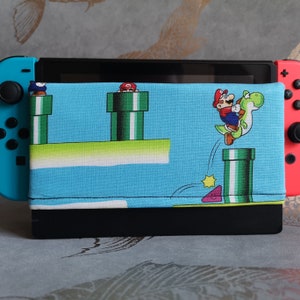 Könnte beinhalten: Eine blaue und grüne Nintendo Switch-Hülle mit Mario-Motiv. Die Hülle zeigt Mario-Charaktere und grüne Rohre.