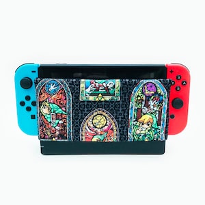 May include: A black Nintendo Switch console with a colorful stained glass design featuring characters from The Legend of Zelda. The design includes a variety of colors, including red, blue, green, yellow, and purple.