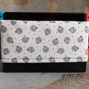 May include: A black Nintendo Switch console with a white and black cupcake pattern fabric case. The console has blue and red Joy-Con controllers.
