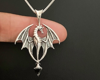 May include: A silver dragon pendant with black wings and a black gemstone. The dragon is in a standing position with its wings spread out.