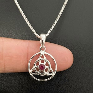 May include: Silver necklace with a circular pendant featuring a Celtic knot design with a red gemstone in the centre.