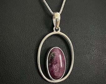 May include: A silver chain necklace with a pendant featuring a purple and black oval gemstone set in a silver oval frame.