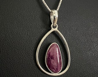 May include: A silver chain necklace with a pendant featuring a teardrop-shaped frame that holds a purple gemstone.