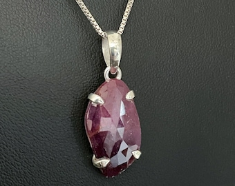 May include: A silver chain necklace with a pendant featuring a large, faceted, pink ruby gemstone.