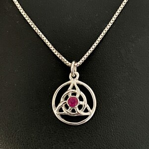 May include: A silver necklace with a pendant featuring a Celtic knot design with a ruby gemstone in the centre.
