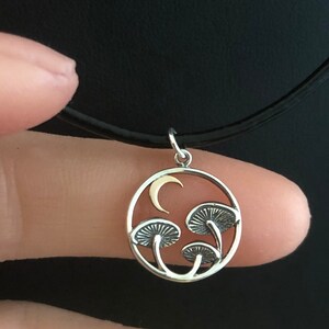 May include: A silver necklace with a circular pendant featuring three mushrooms and a crescent moon. The pendant is made of silver and has a gold crescent moon.