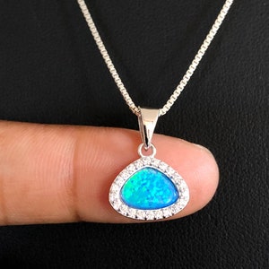 Op de afbeelding: Een zilveren ketting met een hanger met een blauwe opaal steen omringd door een halo van heldere zirkonia stenen.