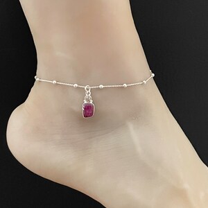 Può includere: Un braccialetto per caviglia in argento con un piccolo ciondolo quadrato di pietra preziosa rosa. Il braccialetto è realizzato con una catena delicata con piccole perle d'argento.