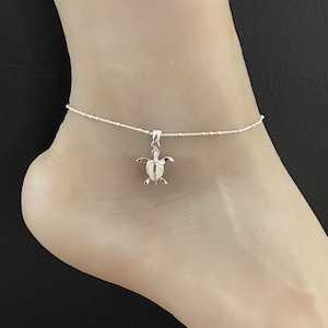 May include: Silver anklet with a small turtle charm. The anklet is made of a delicate chain with small beads.