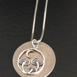 May include: A silver necklace with a pendant featuring a crescent moon and three mushrooms in a circle. The pendant is about the size of a US quarter.