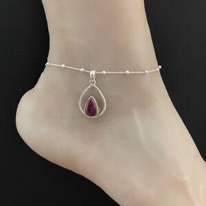 May include: A silver anklet with a teardrop-shaped pendant featuring a purple gemstone.