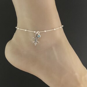 May include: A silver anklet with a small blue gemstone and a silver lizard charm.