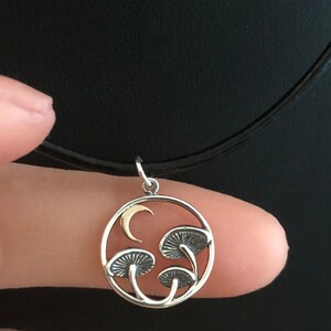 May include: A silver necklace with a circular pendant featuring three stylized mushrooms and a crescent moon. The pendant is made of silver with a gold crescent moon.