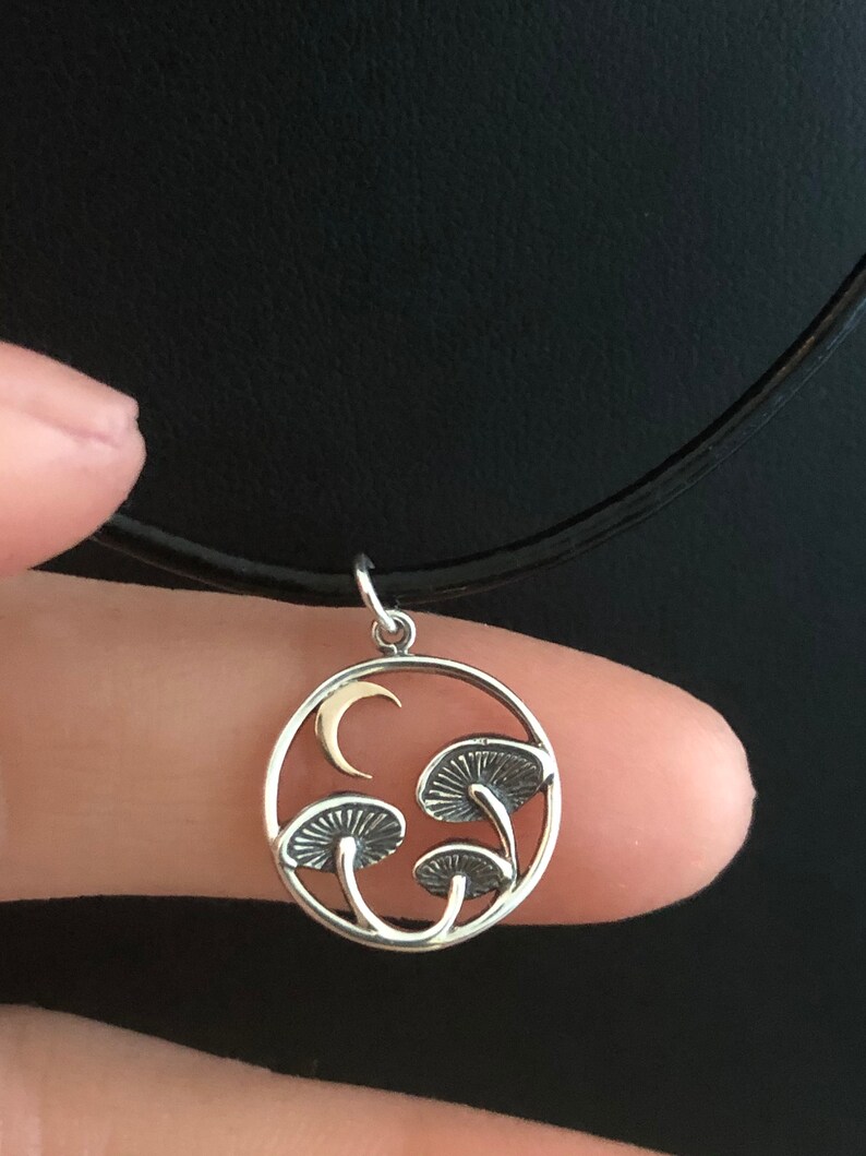 May include: A silver necklace with a circular pendant featuring three stylized mushrooms and a crescent moon. The pendant is made of silver with a gold crescent moon.