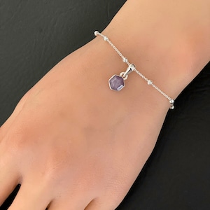 May include: A silver chain bracelet with a small, hexagonal pendant featuring a purple gemstone.