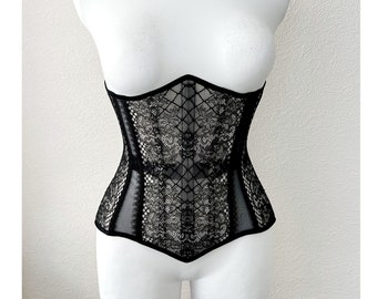 May include: A black lace corset with a pointed bottom and a delicate floral pattern. The corset is on a white mannequin.