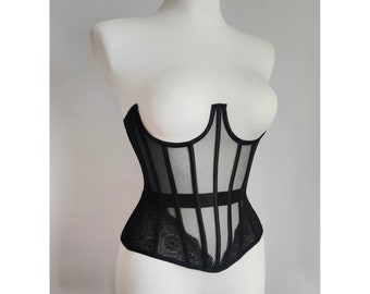 Può includere: Un corpetto in mesh nero con un bordo in pizzo. Il corpetto ha una struttura a stecche e un fondo a punta.
