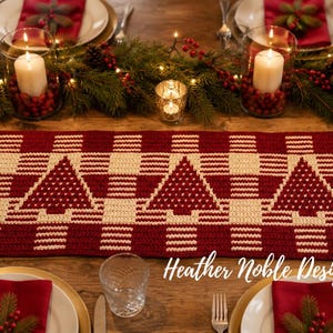 Op de afbeelding: Een rechthoekige gehaakte tafelloper met een herhalend patroon van crèmekleurige kerstbomen tegen een dieprode achtergrond. Het ontwerp bevat een geblokt rastermotief door de hele stof, met de tekst Heather Noble Designs.