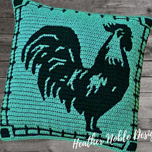 May include: A square, turquoise crochet pillow featuring a black rooster silhouette. The pillow has a black border with a fence design and the text "Heather Noble Designs" in the bottom right corner.