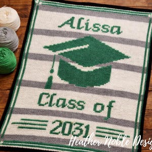 May include: A hand-knitted graduation blanket with a green mortarboard design and the name "Alissa" in green letters. The blanket features the text "Class of 2031" and is bordered in black. The background has grey and white stripes.