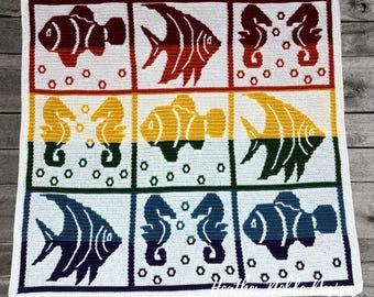 May include: A square crochet blanket featuring a grid of nine panels with marine life motifs including fish, seahorses, and bubbles. The design uses a gradient color scheme transitioning from red and orange to yellow, green, blue, and purple.