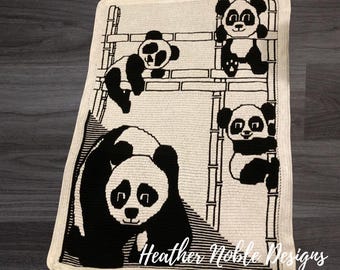 May include: A rectangular crochet blanket featuring a black and white panda theme. The design displays four pandas climbing on bamboo structures, with the text Heather Noble Designs printed in white script at the bottom right corner.