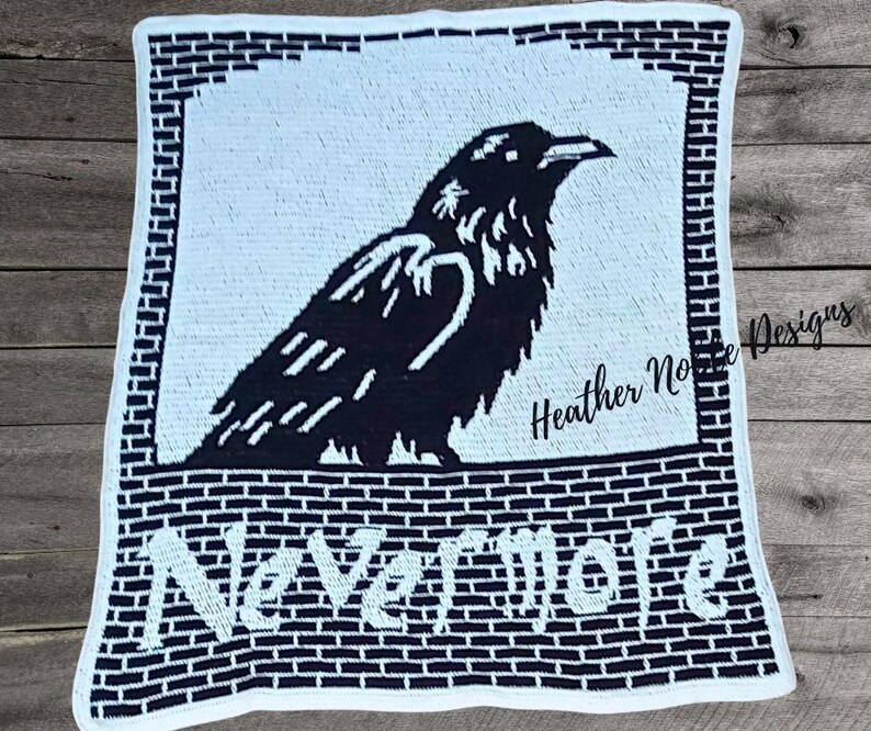 May include: A black and white crochet blanket featuring a raven design. The raven is perched above the word "Nevermore" in white block letters. The blanket has a brick-like border and the text "Heather Noble Designs".