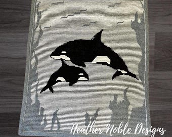 May include: A rectangular crochet blanket featuring a black and white graphic of two orcas swimming. The background consists of horizontal gray and white stripes with darker gray abstract shapes along the edges. The text Heather Noble Designs is visible.