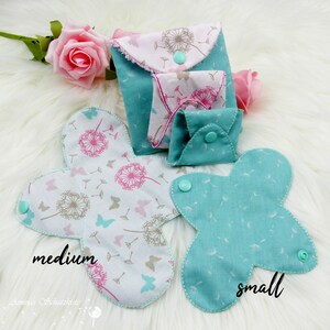 May include: Three reusable cloth menstrual pads in different sizes. The largest pad is white with a dandelion print and the words "medium". The medium pad is turquoise with the word "small". The smallest pad is turquoise with a dandelion print.