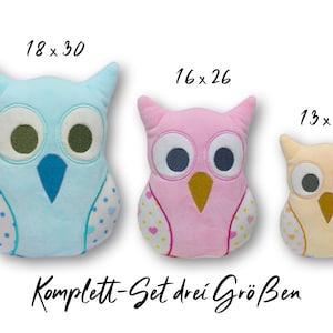 Peut inclure: Ensemble de trois coussins en forme de hibou en peluche de couleur bleue, rose et crème. Les coussins sont décorés de pois blancs et de cœurs. Le plus grand coussin mesure 45,7 cm sur 76,2 cm, le coussin du milieu mesure 40,6 cm sur 66 cm et le plus petit coussin mesure 33 cm sur 45,7 cm. Le texte "Komplett-Set drei Größen" est écrit sous les coussins.