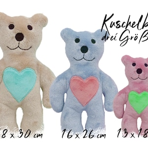 May include: Three plush teddy bears in beige, blue, and pink, each with a heart-shaped patch. The beige bear has a turquoise heart, the blue bear has a pink heart, and the pink bear has a green heart. The bears are 18 x 30 cm, 16 x 26 cm, and 13 x 18 cm.