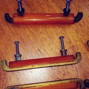 Peut inclure: Ensemble de trois boutons de cabinet en bakélite ambrée vintage avec quincaillerie en laiton et en métal noir.