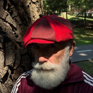May include: A newsboy cap featuring alternating panels of vibrant red corduroy and a dark brown textured fabric. The cap has a structured brim and a multi-paneled crown design, showcasing a distinct contrast between the bright red and dark brown materials.