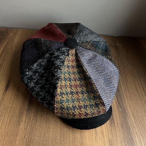 Könnte beinhalten: Eine mehrteilige Newsboy-Cap mit schwarzem Schirm und Knopf. Die Kappe besteht aus verschiedenen Stoffen mit Mustern in Rot-, Schwarz-, Blau- und Goldtönen.